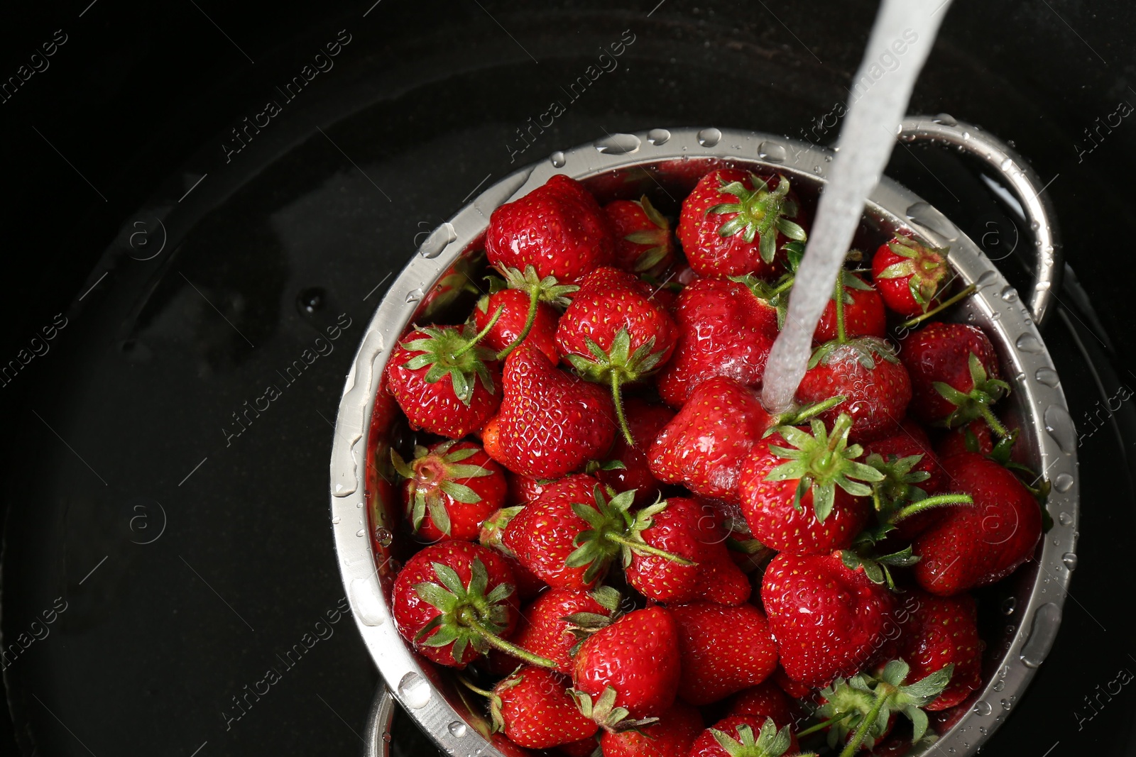 Photo of Washing fresh strawberries under tap water in metal colander in sink, top view