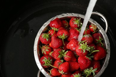 Photo of Washing fresh strawberries under tap water in metal colander in sink, top view