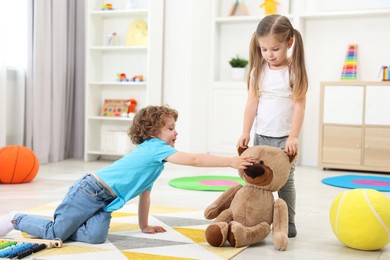 Photo of Cute little children playing with teddy bear on floor in kindergarten