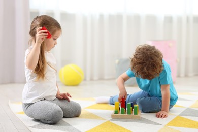 Photo of Cute little children playing with set of wooden geometric figures on floor in kindergarten