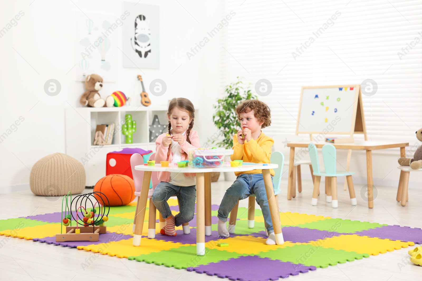 Photo of Cute little children modeling from plasticine at white table in kindergarten