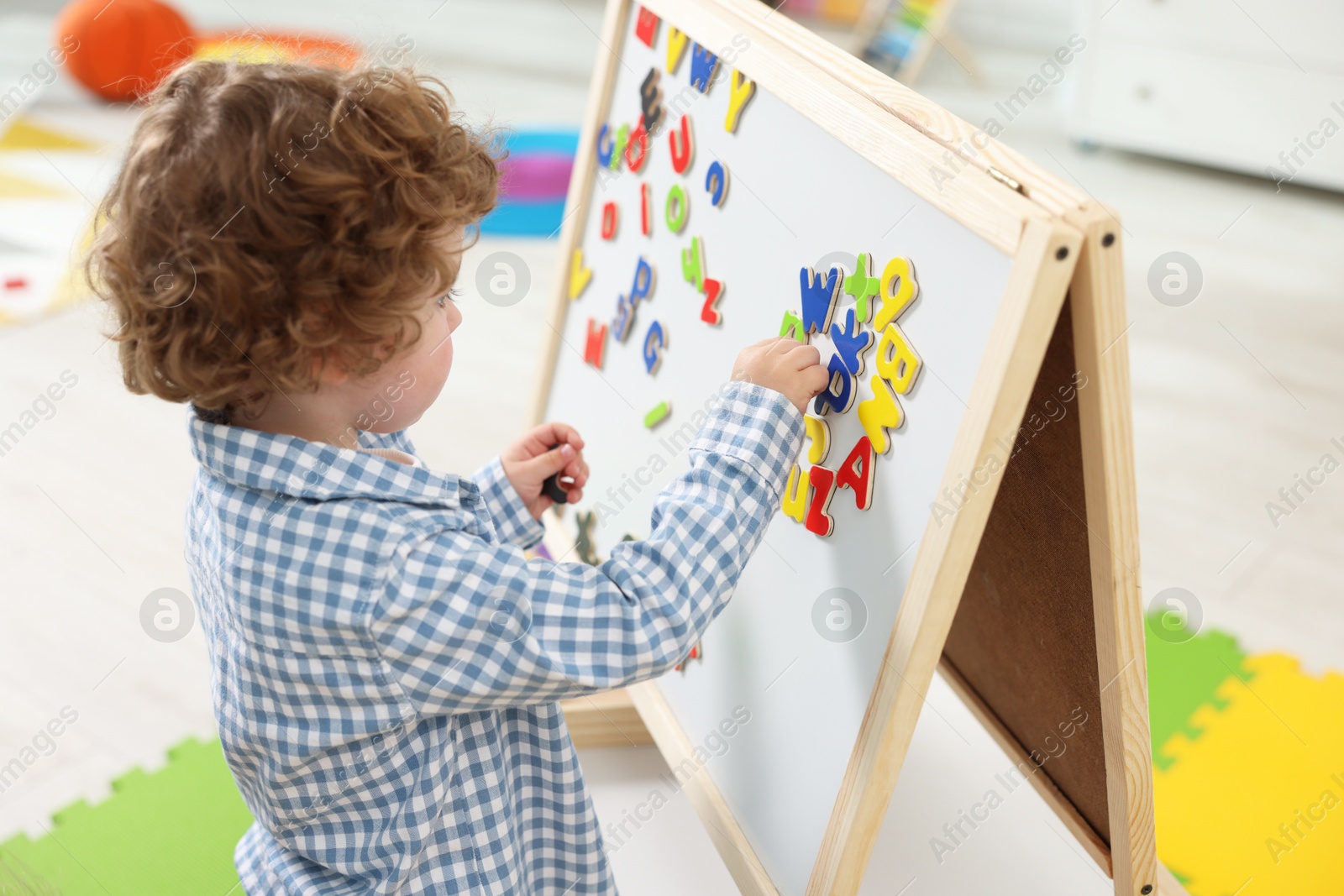 Photo of Cute little boy learning alphabet with magnetic letters on board in kindergarten