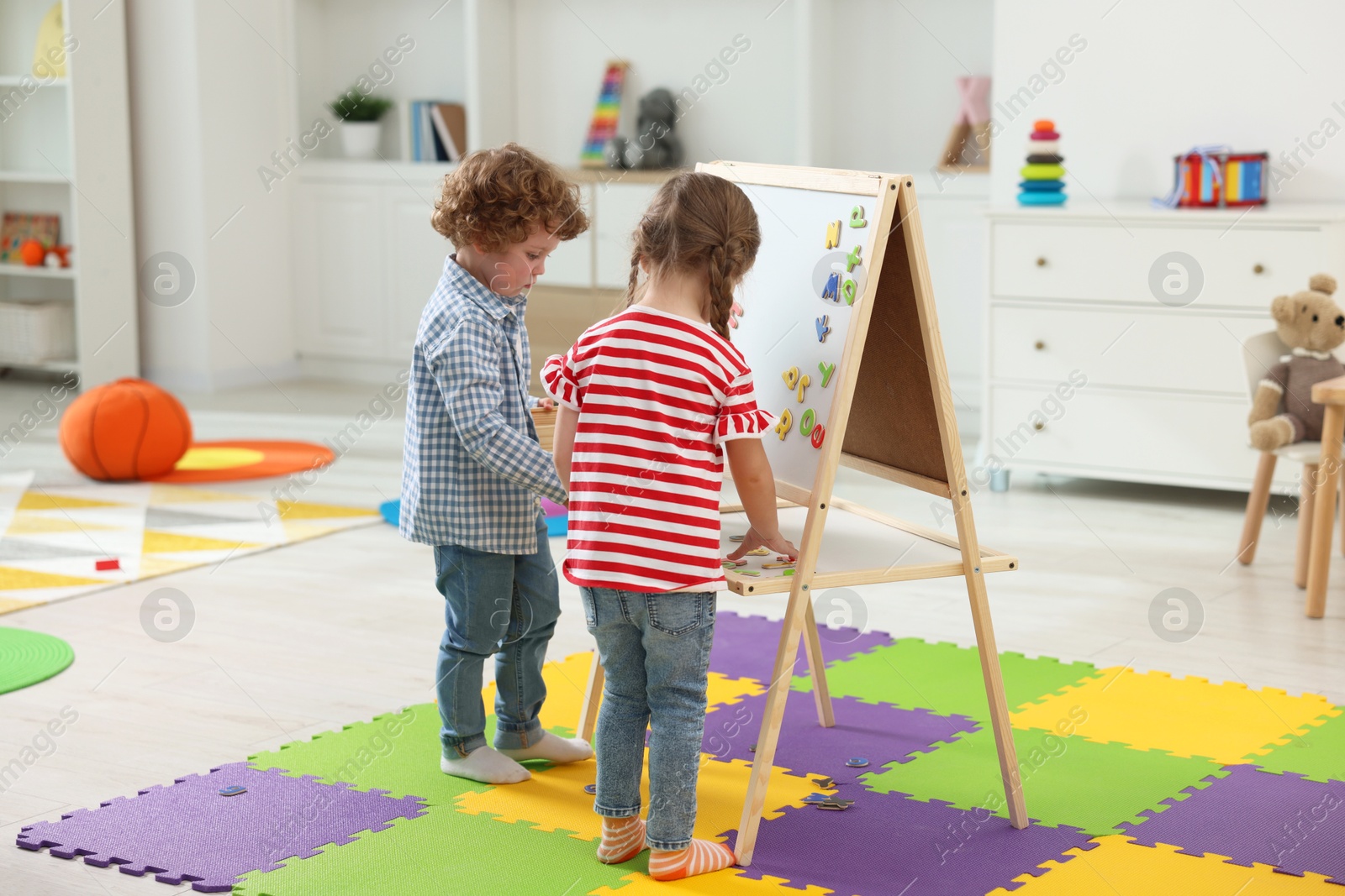 Photo of Little children learning alphabet with magnetic letters on board in kindergarten