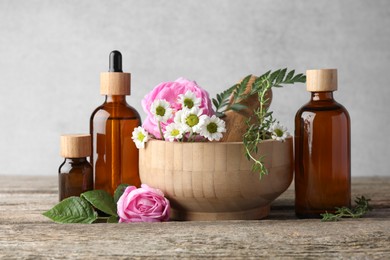 Photo of Aromatherapy. Different essential oils, flowers, mortar and pestle on wooden table