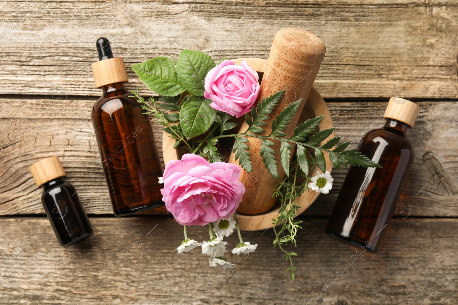 Photo of Aromatherapy. Different essential oils, flowers, mortar and pestle on wooden table, flat lay