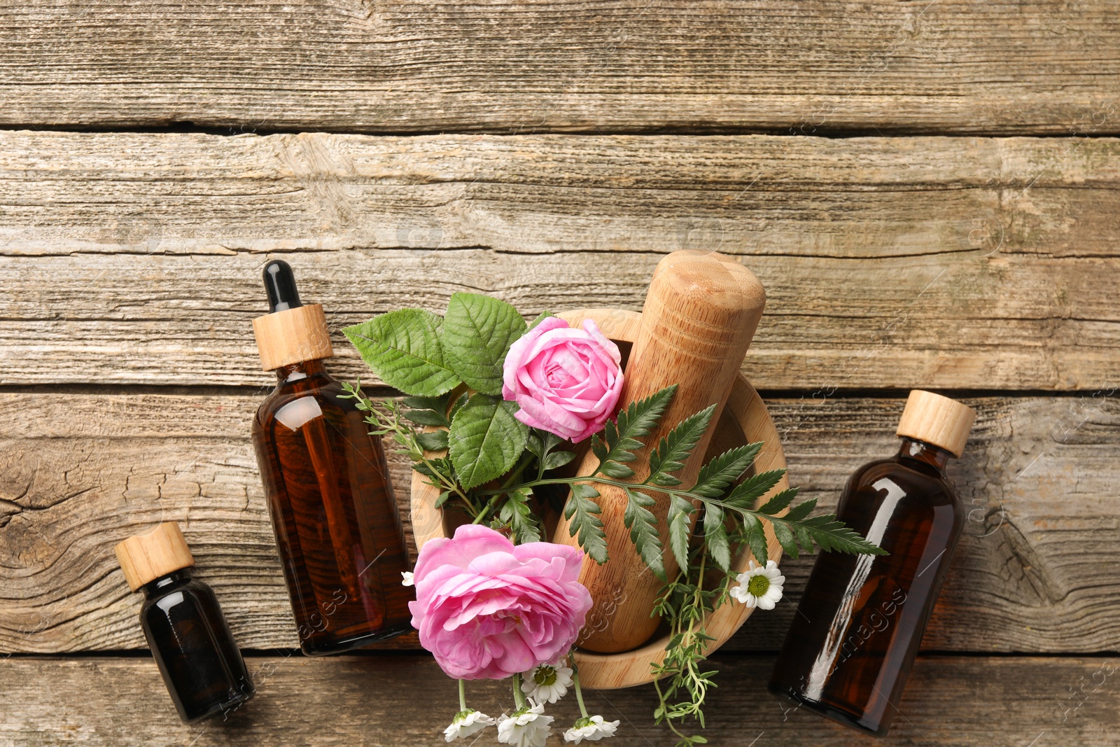 Photo of Aromatherapy. Different essential oils, flowers, mortar and pestle on wooden table, flat lay