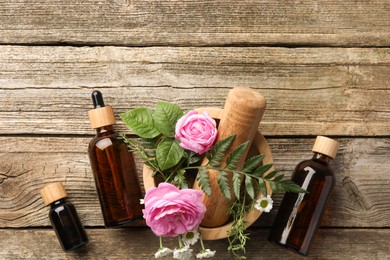 Aromatherapy. Different essential oils, flowers, mortar and pestle on wooden table, flat lay