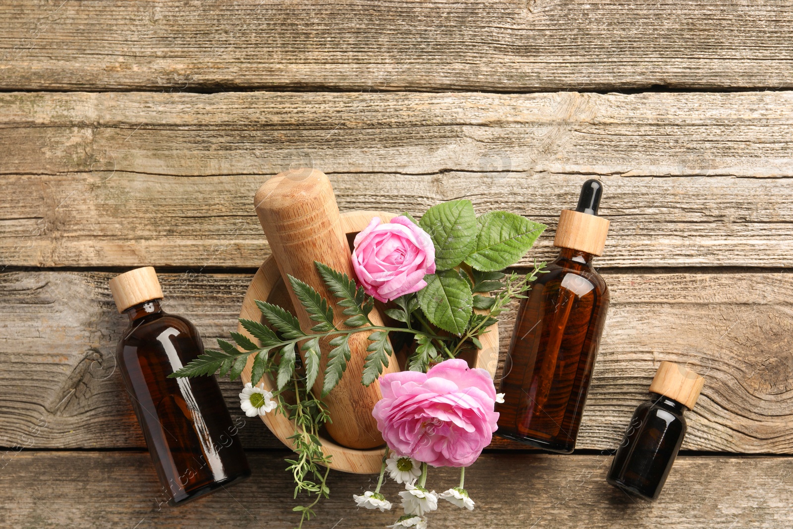 Photo of Aromatherapy. Different essential oils, flowers, mortar and pestle on wooden table, flat lay