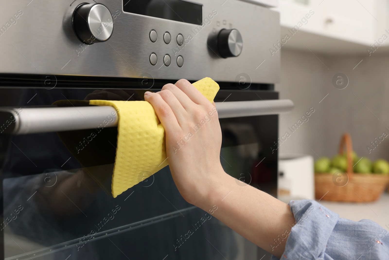 Photo of Woman cleaning electric oven with rag in kitchen, closeup