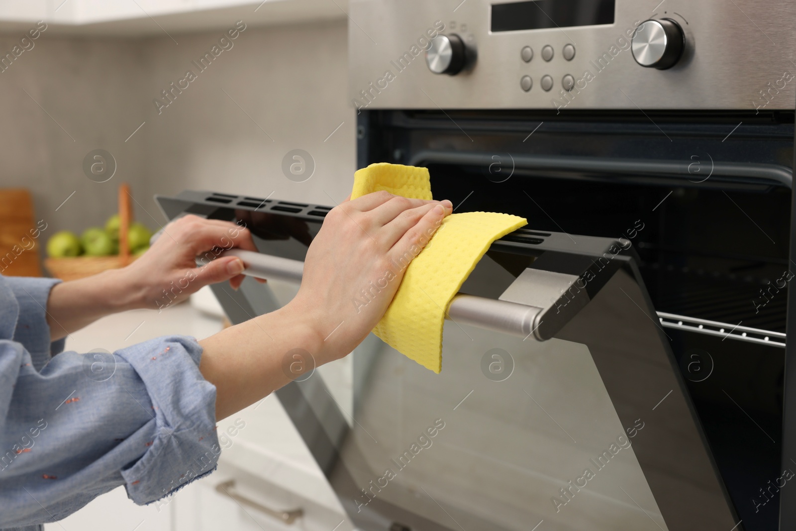 Photo of Woman cleaning electric oven with rag in kitchen, closeup