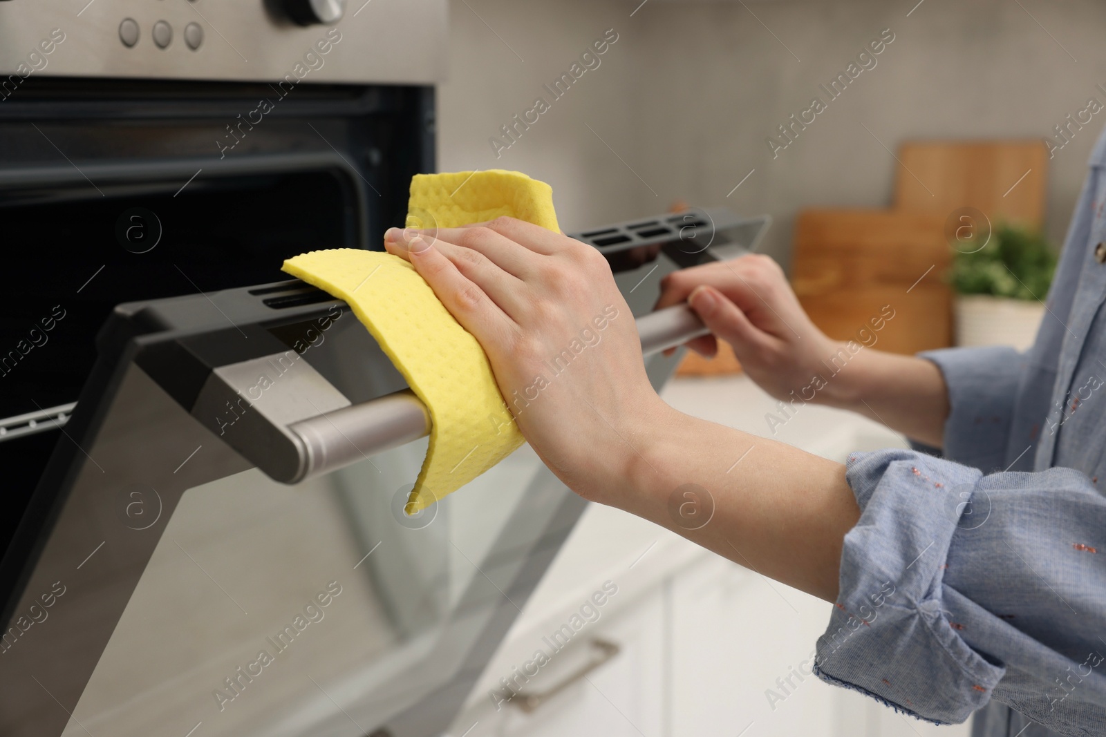 Photo of Woman cleaning electric oven with rag in kitchen, closeup