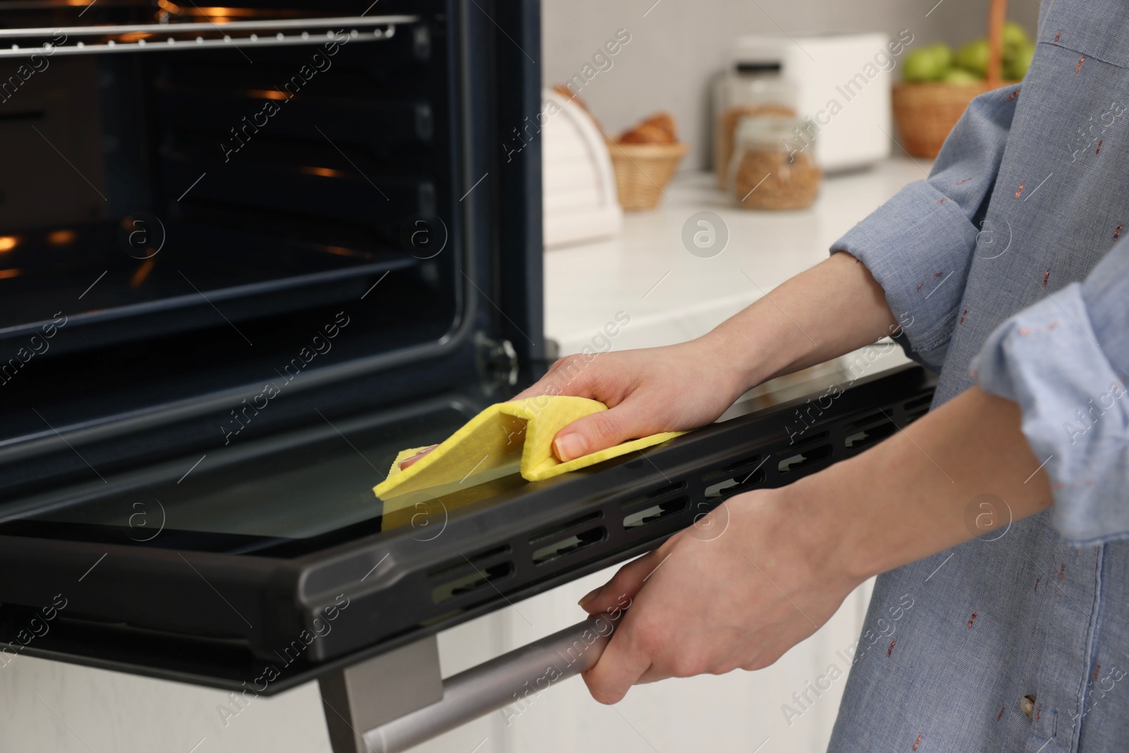 Photo of Woman cleaning oven door with rag in kitchen, closeup