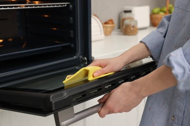 Woman cleaning oven door with rag in kitchen, closeup