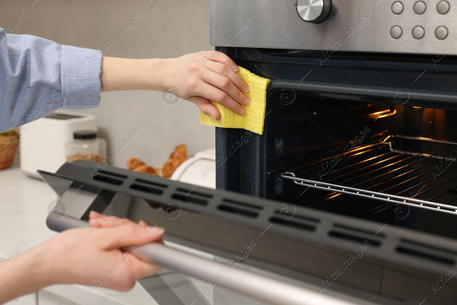 Photo of Woman cleaning electric oven with rag in kitchen, closeup