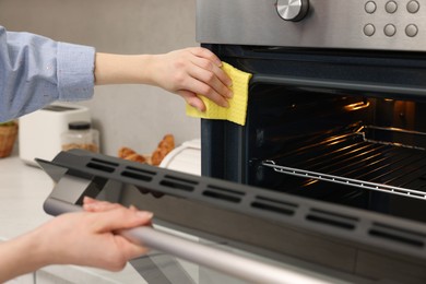 Photo of Woman cleaning electric oven with rag in kitchen, closeup