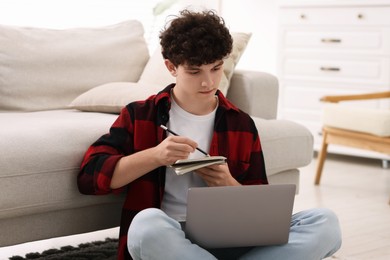 Photo of Teenager taking notes while working with laptop at home. Remote job