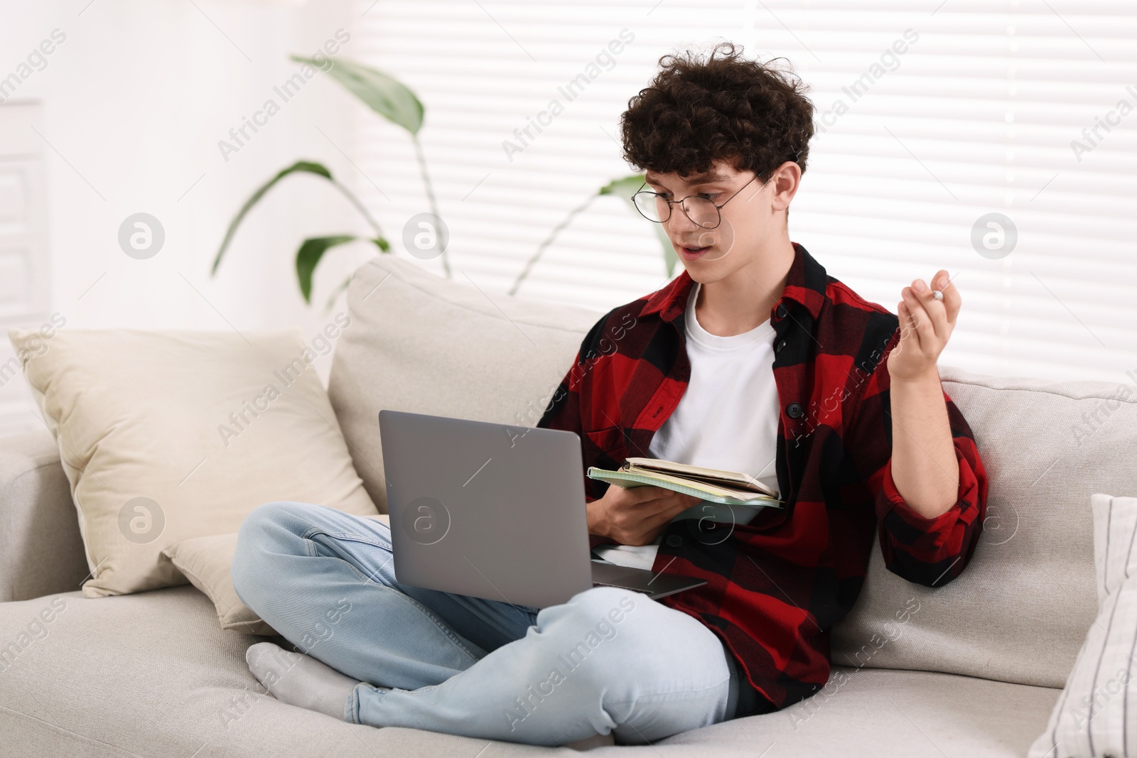 Photo of Teenager with notebooks and pen working on laptop at home. Remote job