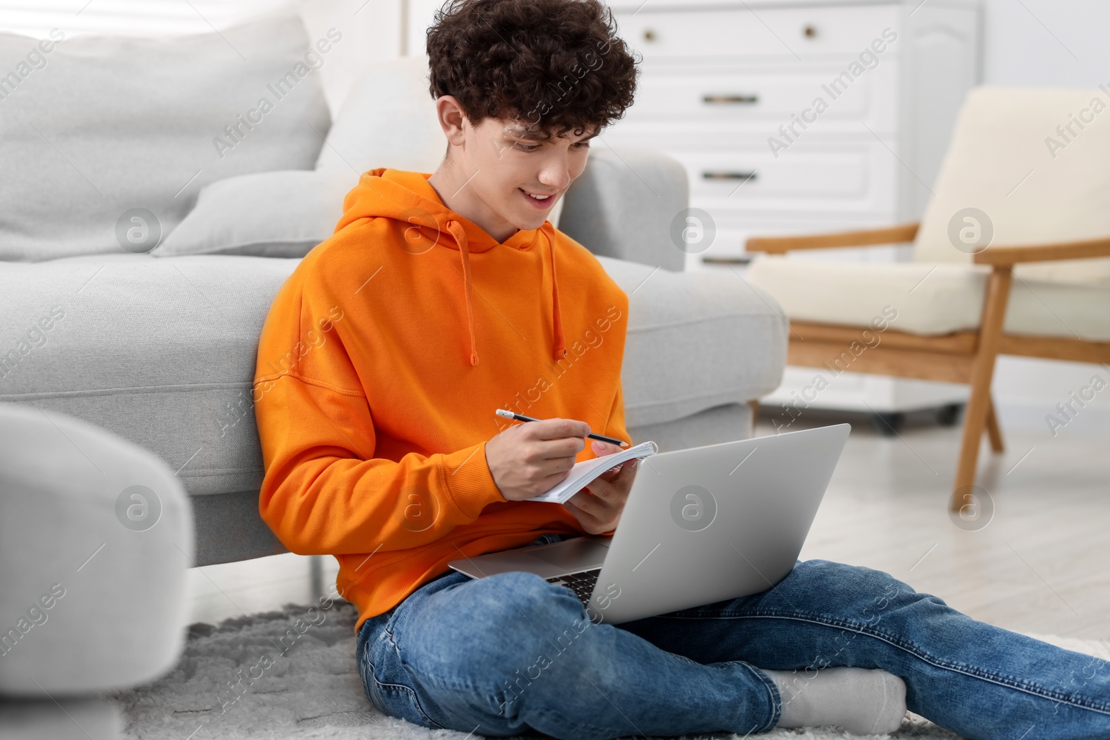 Photo of Teenager taking notes while working with laptop at home. Remote job