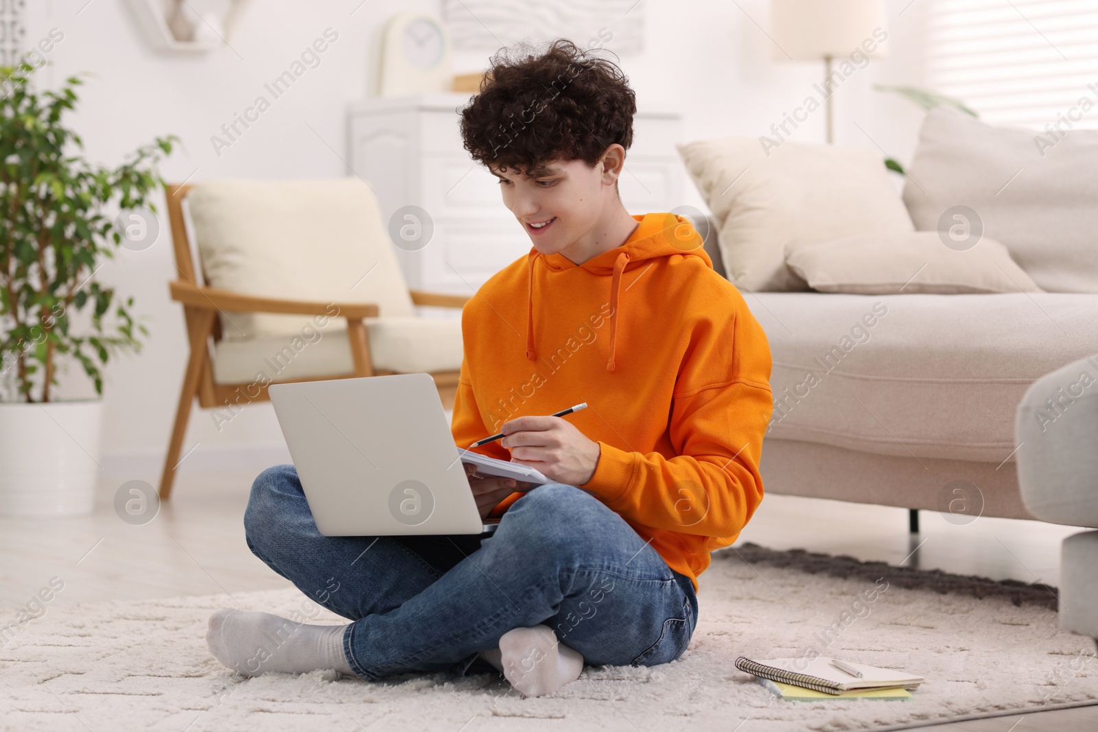 Photo of Teenager taking notes while working with laptop at home. Remote job