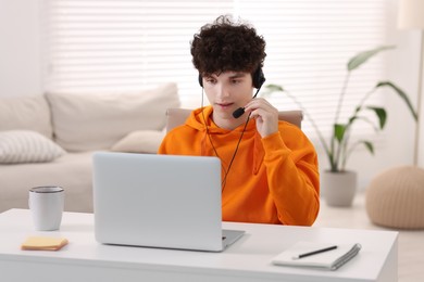 Photo of Teenager in headset working with laptop at home. Remote job