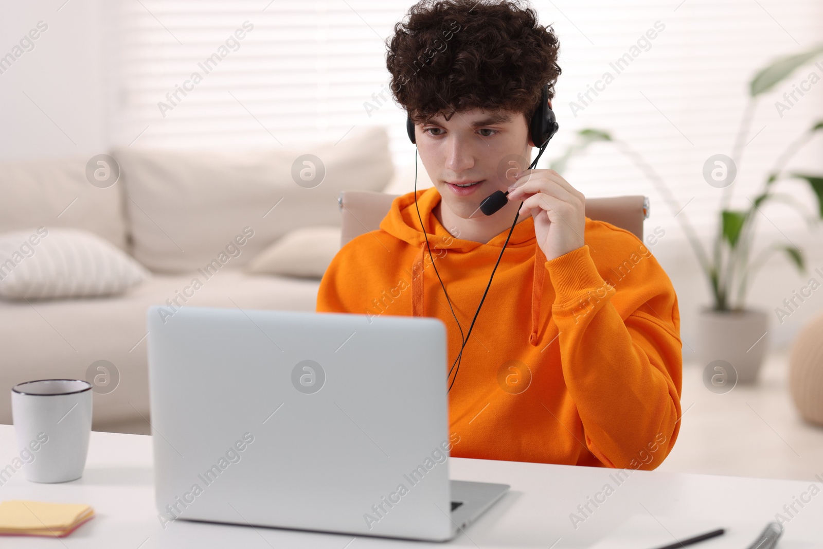 Photo of Teenager in headset working with laptop at home. Remote job