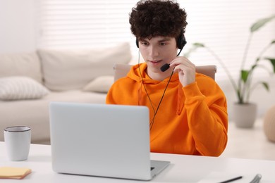 Photo of Teenager in headset working with laptop at home. Remote job