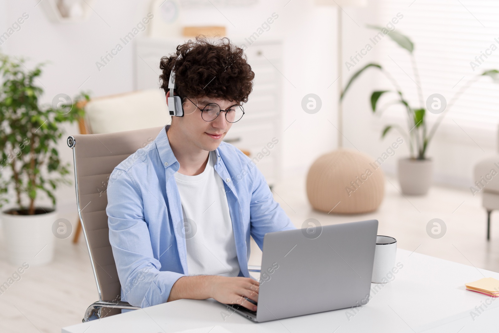 Photo of Teenager in headphones working with laptop at home. Remote job