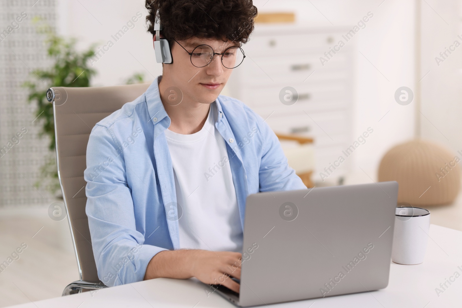 Photo of Teenager in headphones working with laptop at home. Remote job