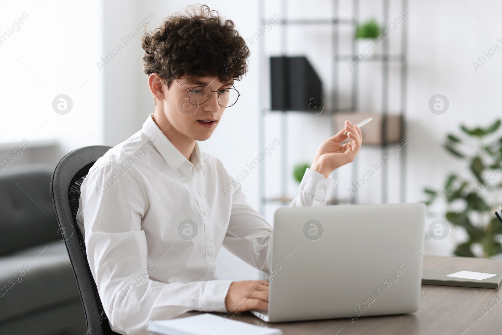 Photo of Teenager with pen working on laptop at table indoors. Remote job