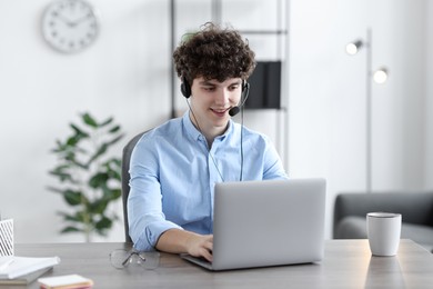 Teenager in headset working with laptop at table indoors. Remote job