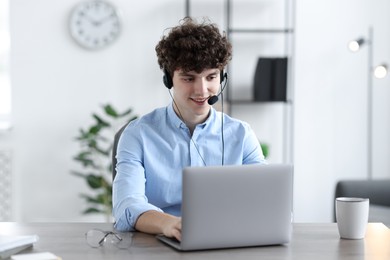 Photo of Teenager in headset working with laptop at table indoors. Remote job