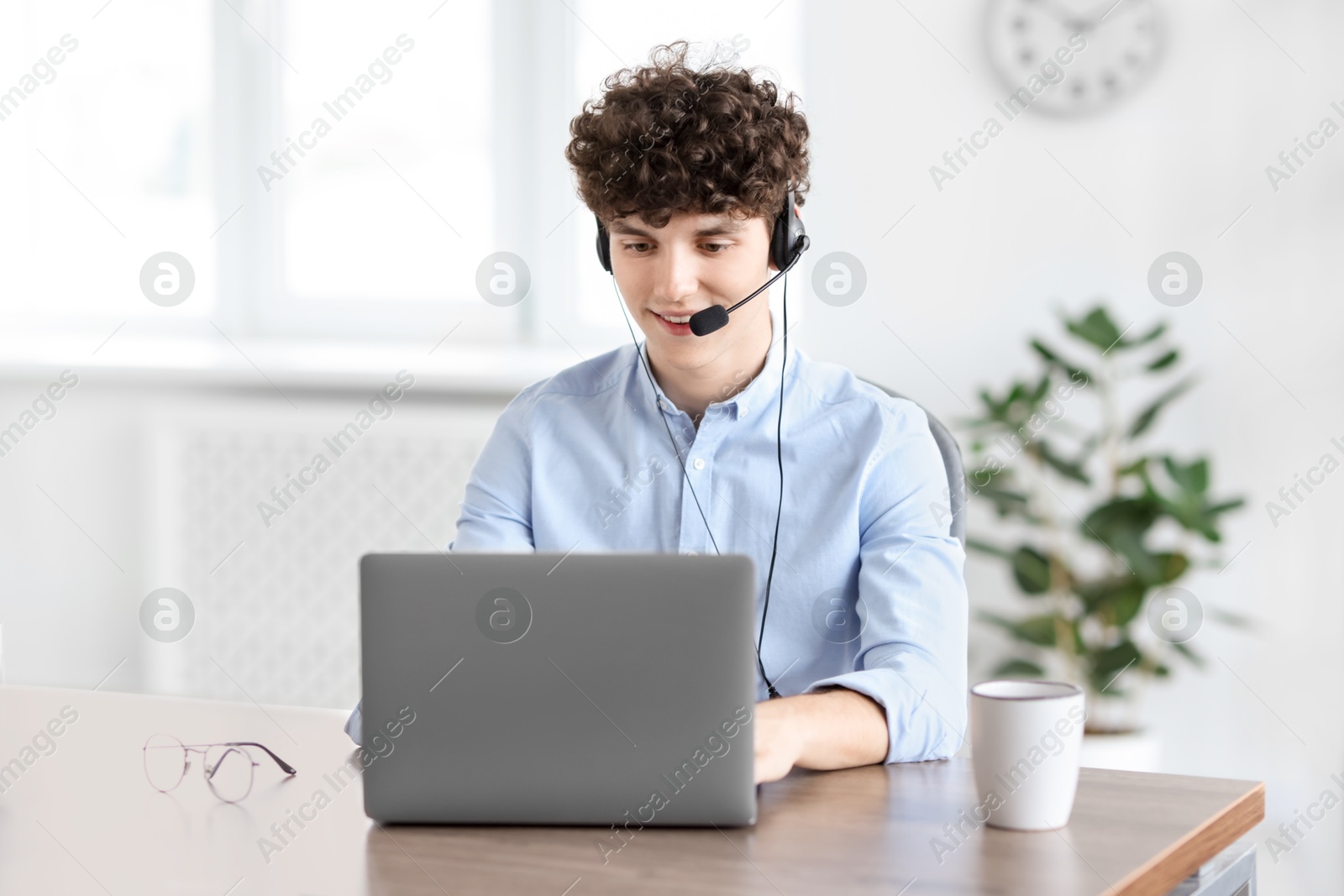 Photo of Teenager in headset working with laptop at table indoors. Remote job