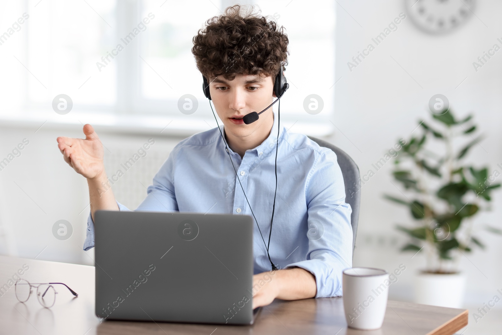 Photo of Teenager in headset having video chat via laptop at table indoors. Remote work