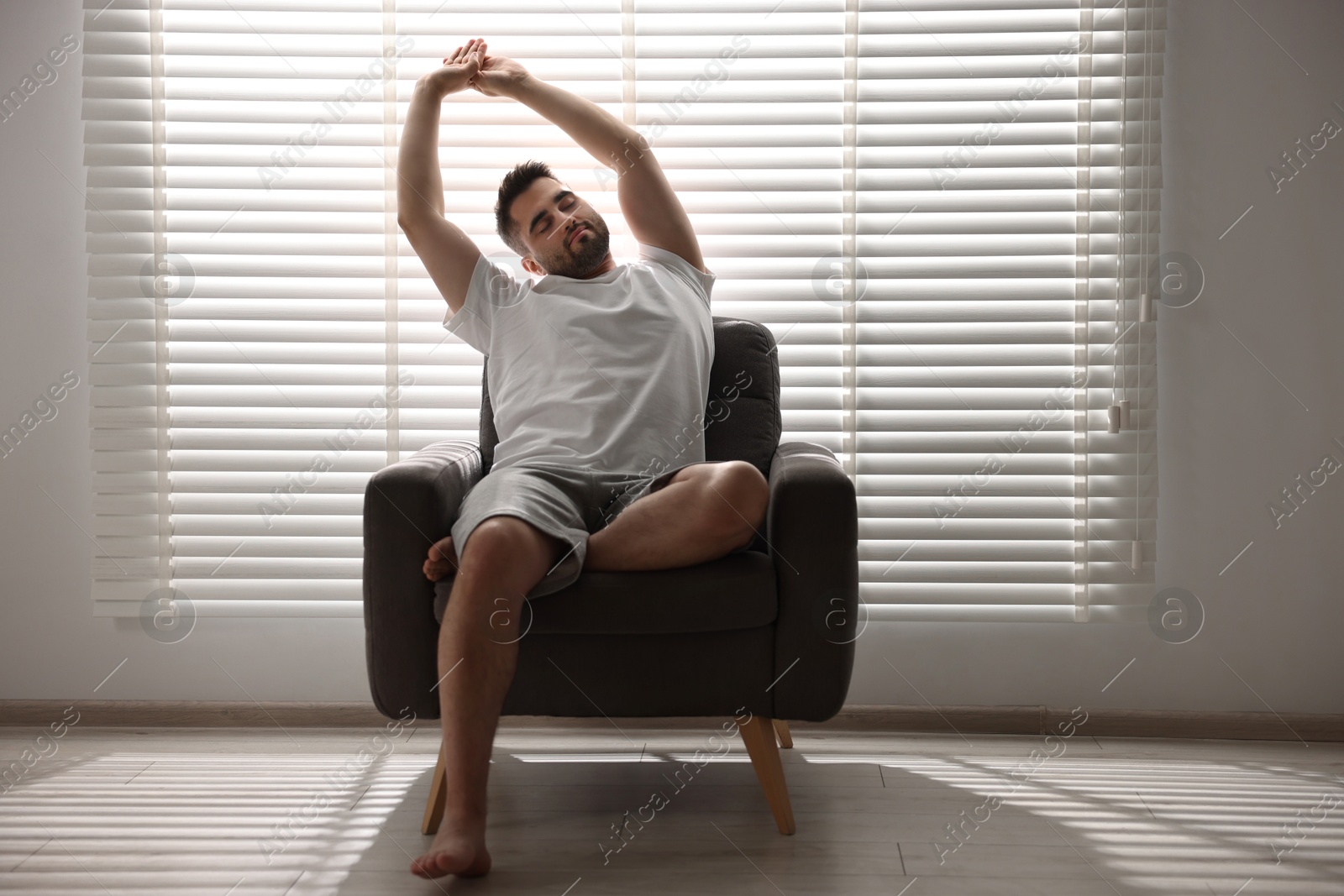 Photo of Man sitting on armchair near window blinds indoors