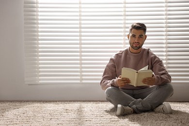 Photo of Man reading book near window blinds at home, space for text