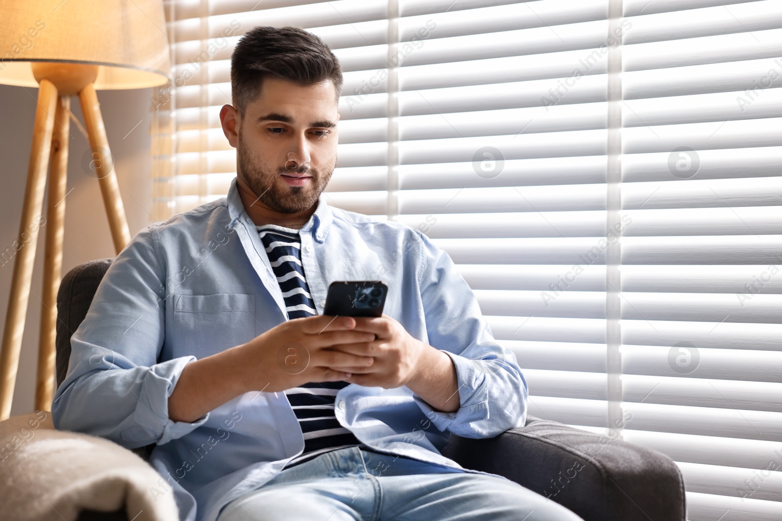 Photo of Man using smartphone near window blinds at home