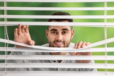 Photo of Young man looking through window blinds on blurred background