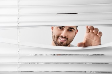 Photo of Young man looking through window blinds, space for text