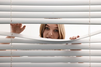 Photo of Young woman looking through window blinds on white background