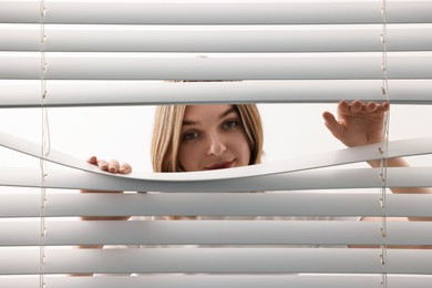 Young woman looking through window blinds on white background