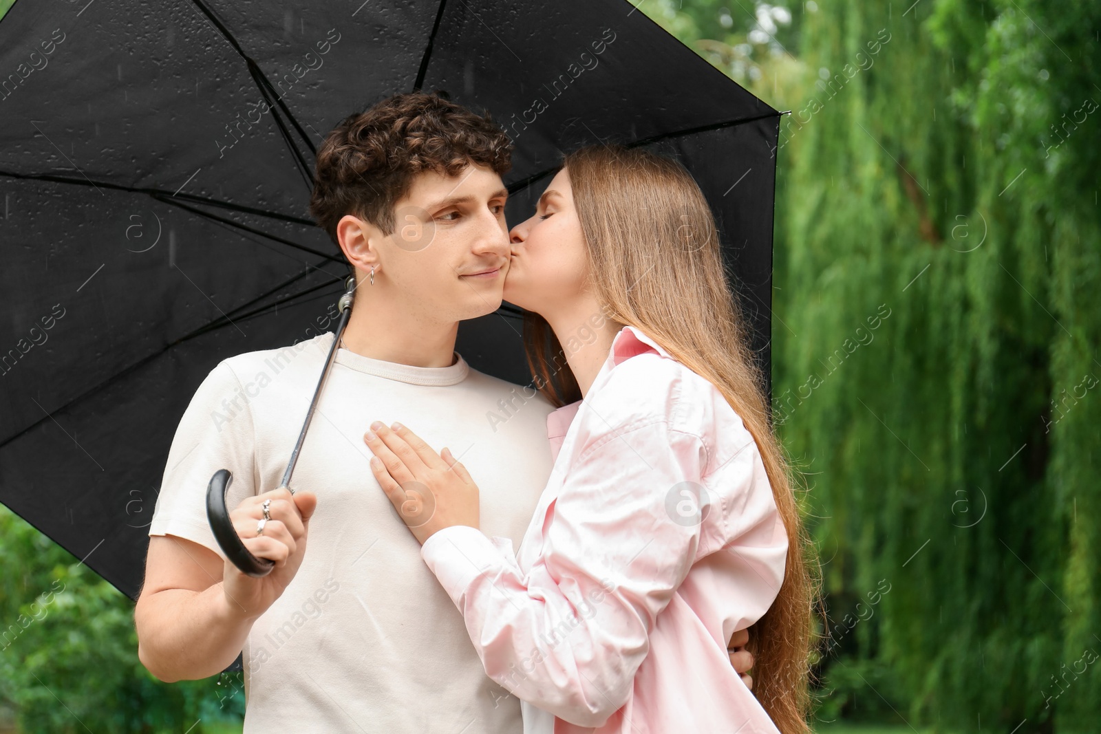 Photo of International dating. Lovely young couple with umbrella spending time together in park