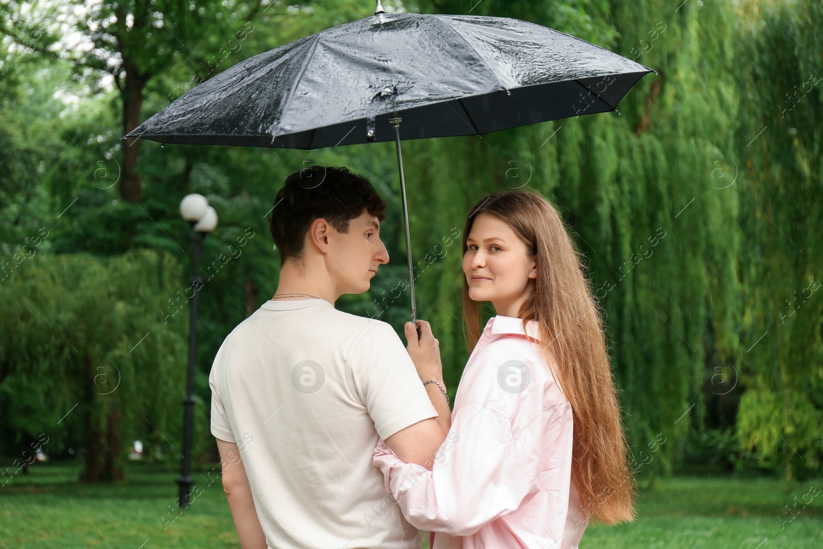 Photo of International dating. Lovely young couple with umbrella spending time together in park