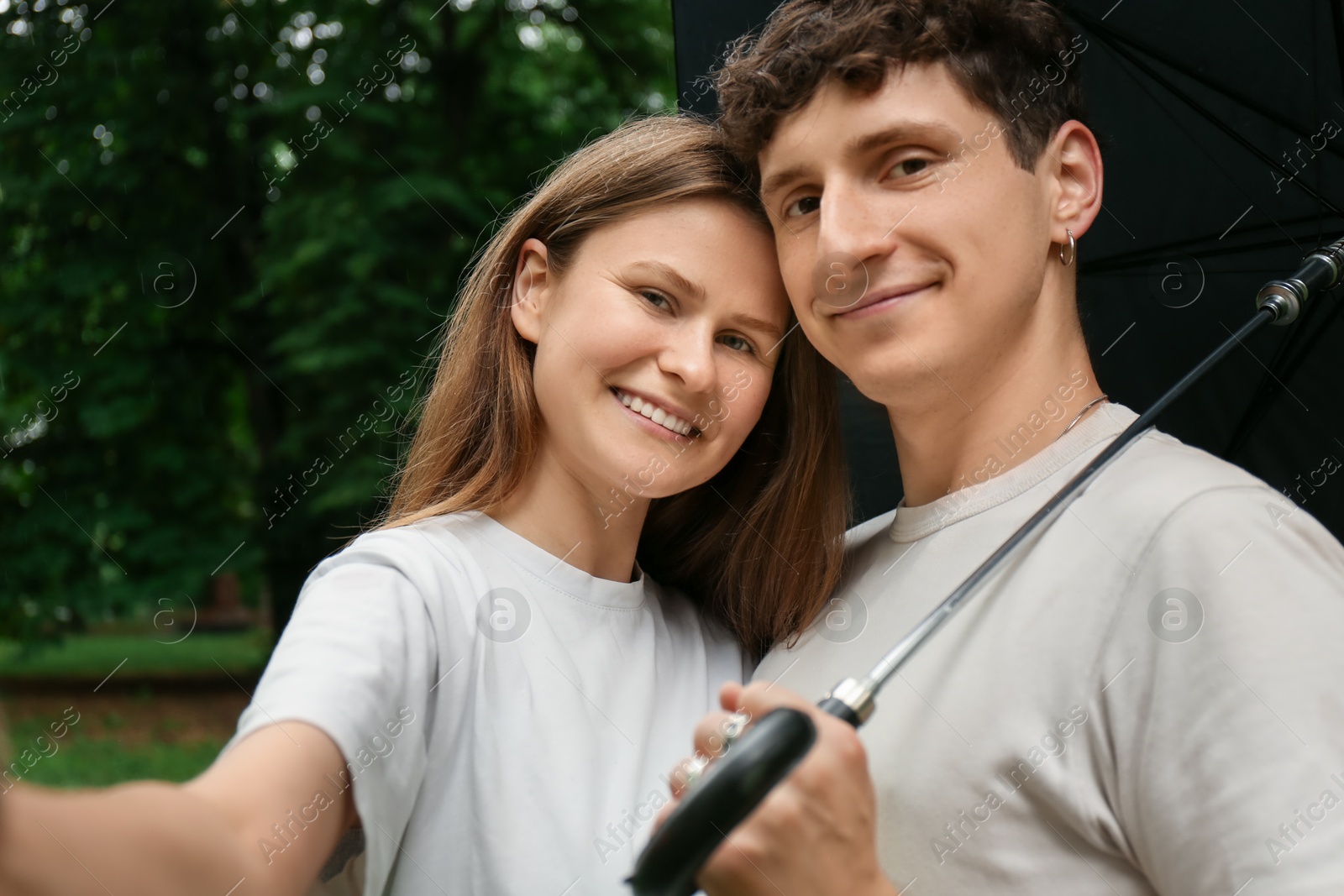 Photo of International dating. Lovely young couple with umbrella taking selfie and spending time together in park