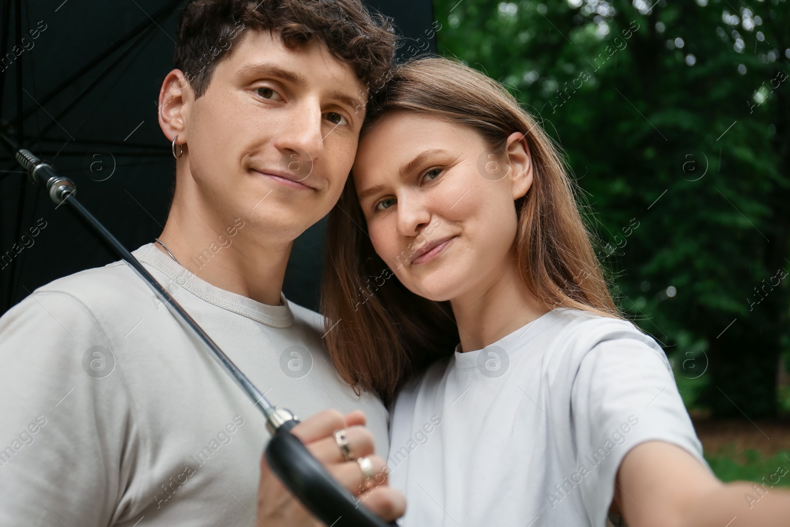 Photo of International dating. Lovely young couple with umbrella taking selfie and spending time together in park