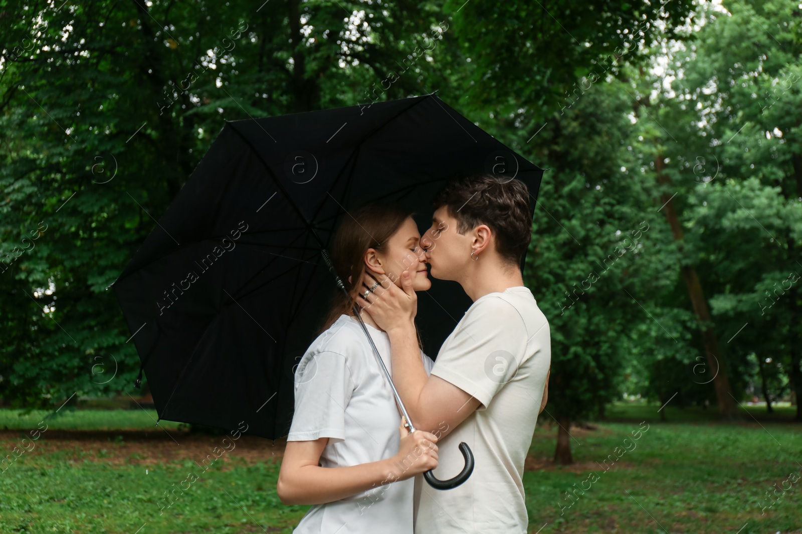 Photo of International dating. Lovely young couple with umbrella spending time together in park