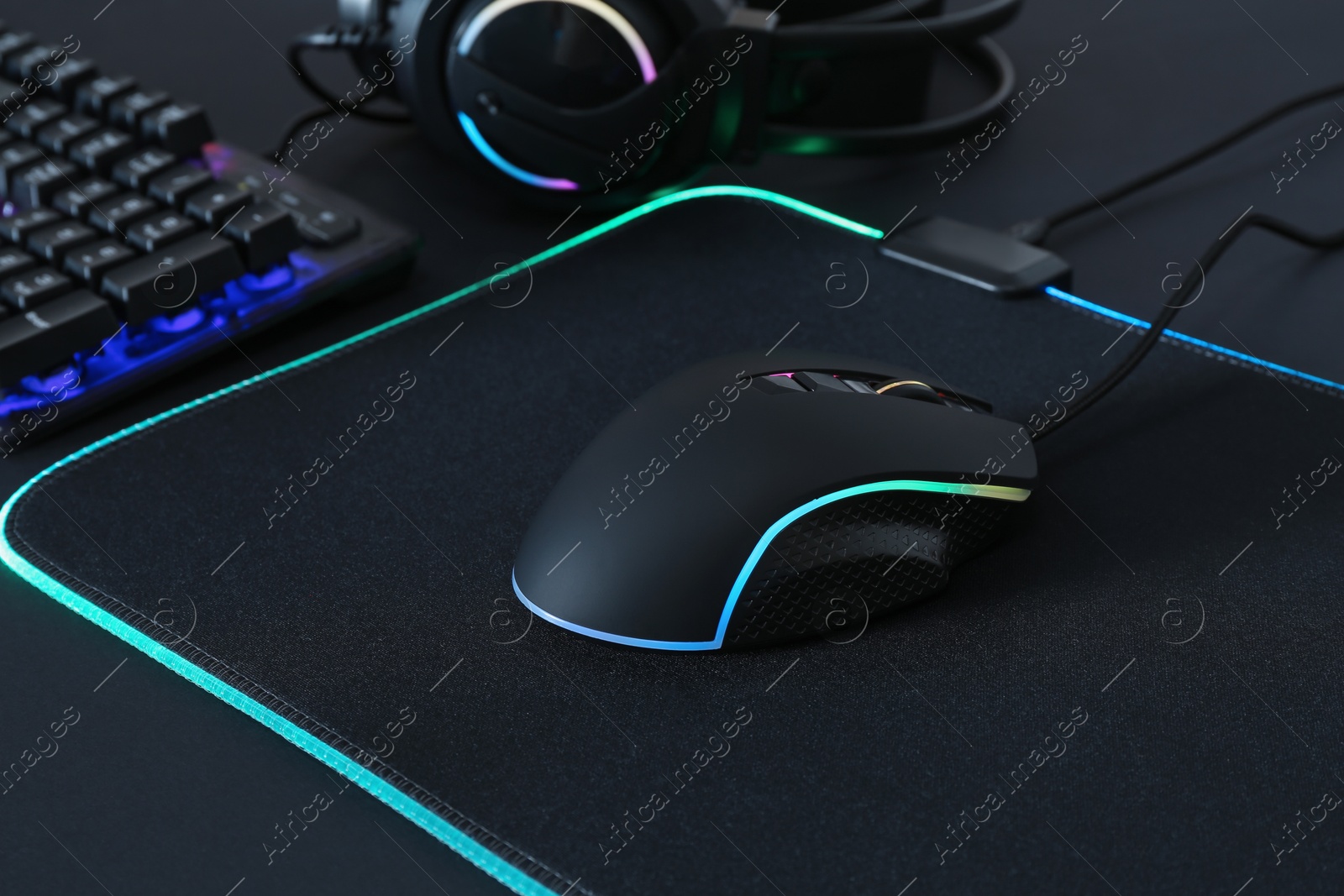 Photo of Computer mouse, mousepad, RGB keyboard and headset on black background