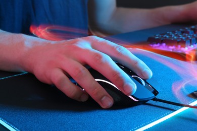 Gamer using modern wired computer mouse in neon lights at dark table, closeup