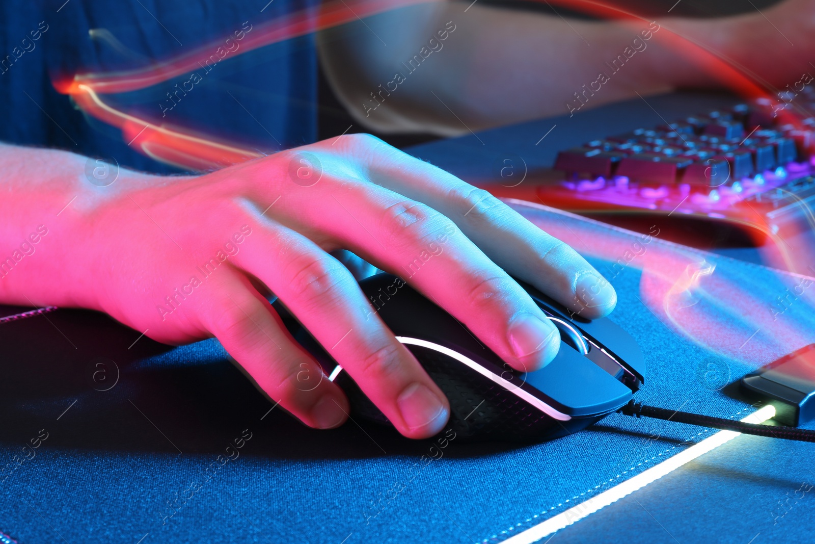 Photo of Gamer using modern wired computer mouse in neon lights at dark table, closeup