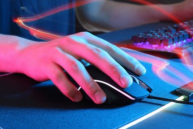 Gamer using modern wired computer mouse in neon lights at dark table, closeup