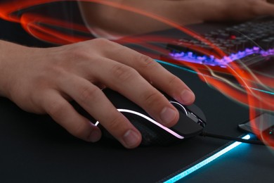 Photo of Gamer using modern wired computer mouse in neon lights at dark table, closeup